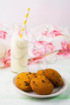 Milk bottle and cookies on white plate, vertical. Sweet pastry. Sweet dessert. Breakfast cookies