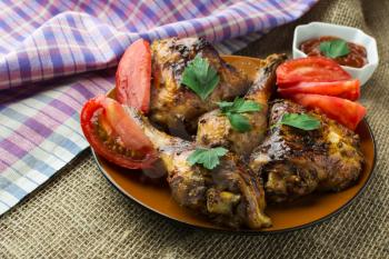 Roasted chicken wings and legs with pieces of tomato and red sauce