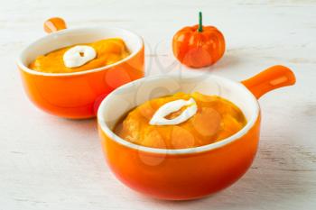 Two portions of pumpkin squash vegetable soup with cream in a orange serving plate with handle, close up