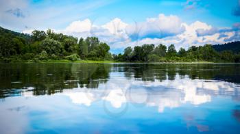 Beautiful landscape panorama with cloudy blue sky reflected in the clear water. Wooded waterside of a mountain lake. Summer idyllic beautiful landscape.