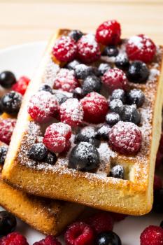 Belgian waffles with fresh berries powdered by caster sugar. Breakfast waffles with blueberry, raspberry and blackcurrant. 
