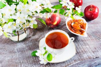 Cup of tea on wooden table and apple jam. Tea time concept. Breakfast tea cup served with flowers.
