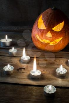 Halloween pumpkin smiling jack-o-lantern and burning candles on dark wooden background, vertical, copyspace