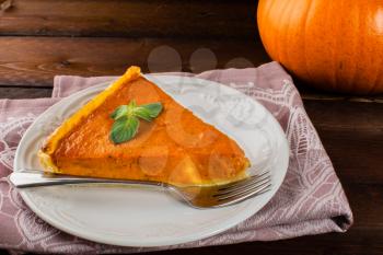A piece of pumpkin pie with mint, white plate, fork, linen napkin on dark wooden background 