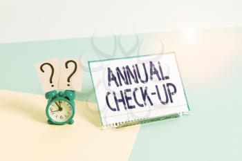Text sign showing Annual Check Up. Business photo showcasing a thorough physical medical examinantion held every year Mini size alarm clock beside a Paper sheet placed tilted on pastel backdrop