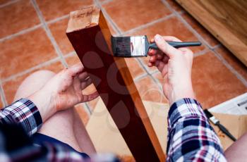 Man holds painting brush and paints wooden board. Top view of hands holding painting brush. Closeup view of home renovating and old furniture painting