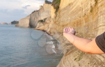 Man extending his hand in a blurry background. Waves shoaling in the seaside. Long ranges of  mountainous cliff. Vertical exposure of rock formation.  Extreme adventure