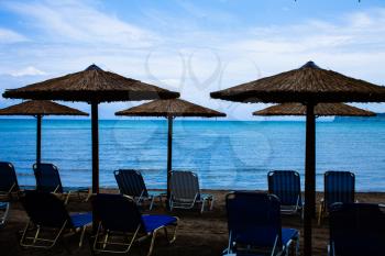 Five Rustic Palapa Umbrellas located at the shoreline of the mediterranean sea with Folding Blue Chairs over the Sand, Vacation Landscape at the Beach with sun loungers and parasols