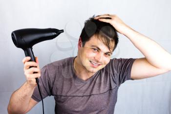Young man dries hair with an electric fan. Preparing a haircut for going to a night life.Man holding hair blower. Teenager smiling while he dries his hair.