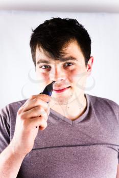 Handsome young man removes nose hair with electric shaver. Young man remove hair from his nose with trimmer. Beauty and people concept. Male cutting hairs in the nose using electric trimmer