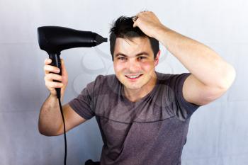 Teenager smiling while he dries his hair. Man holding hair blower. Young man dries hair with an electric fan. Preparing a haircut for going to a night life