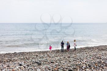 The family is walking along the beach by the sea. Family concept with kids. Wind on the seashore with people walking on the beach. Rocky beach by the sea.