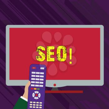 Conceptual hand writing showing Seo. Concept meaning Search engine optimization increase in online marketing channel Hand Holding Remote Control infront of Wide Color PC Screen