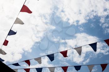 Multicolored Triangular Flags Hanging in the Sky at an Outdoor. Garland of bright colored developing in the wind against the background of the cloudy sky
