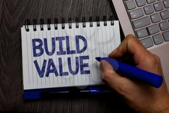 Writing note showing Build Value. Business photo showcasing efficient enough way that it will generate profit after cost Man holding marker spiral notebook computer keyboard wooden background