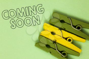 Text sign showing Coming Soon. Conceptual photo something is going to happen in really short time of period Three green yellow vintage clothespins clear background Holding things