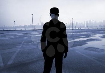 Man in classic black suit stands on empty parking lot. Modern city at the horizon