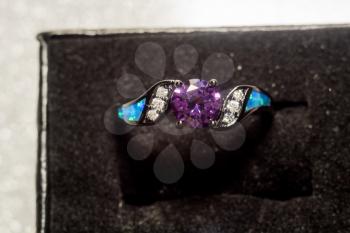 Fashion black gold ring with purple amethyst on glittering background.