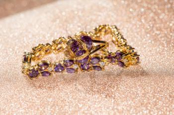 Decorative golden bracelet with purple amethysts on glittering background.