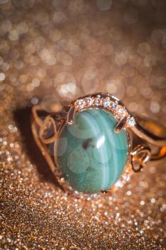Modern gold ring decorated with green striped agate on glitter background.