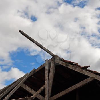 Collapsed wooden roof of an abandoned house and cloudy sky.