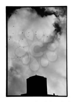 Church silhouette under cloudy sky and flock of flying birds. Old black and white photo darkroom print with dust and scratches, Meteora, Greece circa 1990.