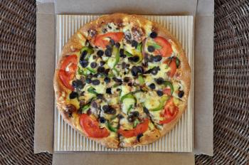 Vegetarian pizza with tomato, olives, pepper, mushrooms and onions packaged in cardboard box. Italian takeaway food background. 