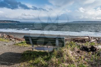 The normally placid Puget Sound is filled with whitewater on a windy day. Bench in the foreground.