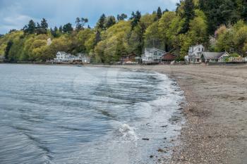 Small waves ripple toward shore at Dash Point Washington. Homes sit under lush green trees as Spring erupts in the Pacific Northwest.
