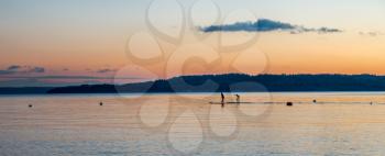 Two paddle boarders move across the Puget Sound at sunset with Mount Rainier in the distance.