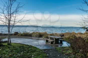 A picnic table sits on shore at Seahurst Park in Burien, Washington. The Olympic Moountains can be seen across the Puget Sound.