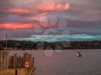 A boat is anchored at Three Tree Point, Washington as the sun sets.  A pink and purple sky blankets the Puget Soiund.