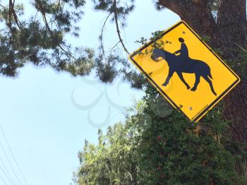 Horse crossing sign yellow with green trees and blue sky