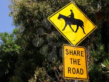 Horse crossing sign yellow with green trees near roadside
