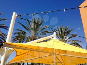 Yellow mesh canvas shade canopies and palm trees on sunny day