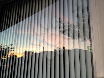 Glass window reflection of sunset with vertical blinds and mountain horizon clouds