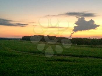sunset over green grassy farm field with strange cloud of steam amoke