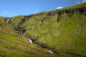 Landscape of Faroe Islands showing blue sky, green mountains and waterfall