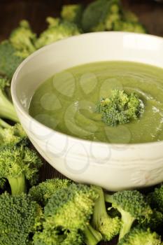 Broccoli soup in a white bowl with fresh vegetables