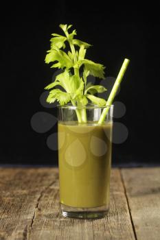 Glass with green juice, celery branch and straw.