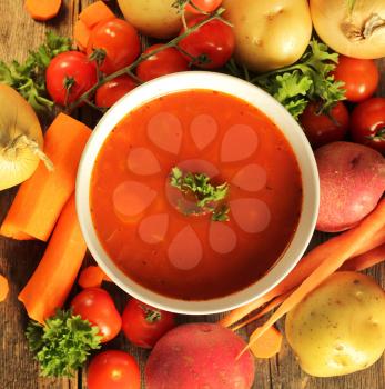 Vegetables soup surrounded by fresh vegetables and a spoon on a wooden background