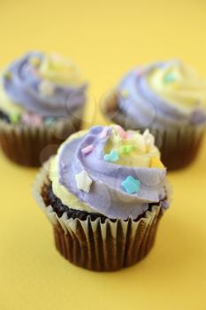 Three easter yellow and lilac chocolate cupcake with candies on a yellow and purple background