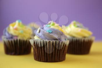 Three easter yellow and lilac chocolate cupcakes with candies on a yellow and purple background