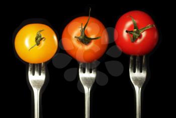 Three tomatoes with different colors on a fork on a black background.  Vegetables are in focus.