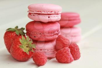 Strawberry and raspberry macarons on a white table with fresh fruits 