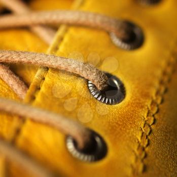 Close up of eyelet and lace on a leather yellow shoe.  Only the middle eyelet in focus.