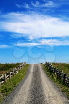 Gravel road surrounded by cedar fence going into a blue sky