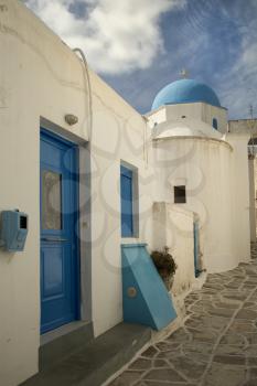 Little alley on Paros island with a white and blue church at the end