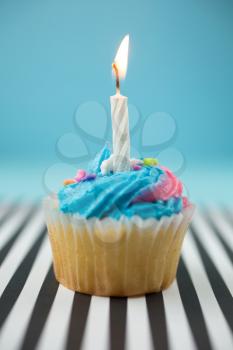 Birthday cupcake with candle and blue and pink icing on a black and white lined background
