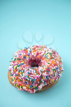 Donut with pink icing and candies on a blue pastel background